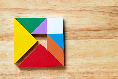 Color tangram puzzle in square with arrow inside shape on wood backgroundの写真素材