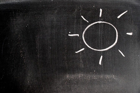 Hand drawing of white chalk in sun shape with copy space on black board backgroundの写真素材