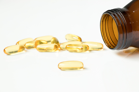 Transparent yellow soft gelatin capsule with amber glass bottle on white backgroundの写真素材