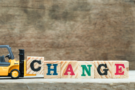 Yellow toy forklift hold letter block C to complete word change on wood backgroundの写真素材