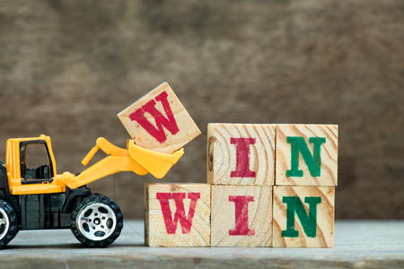 Yellow toy bulldozer hold letter block W to complete word win win on wood backgroundの写真素材