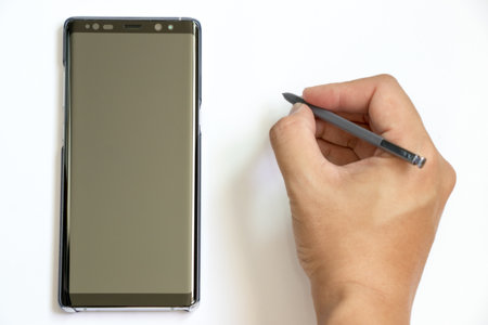BANGKOK, THAILAND - December 23, 2017 : Business man hold the stylus to write at Samsung Galaxy Note 8 on white background. It is the flagship smartphone with android os.のeditorial素材