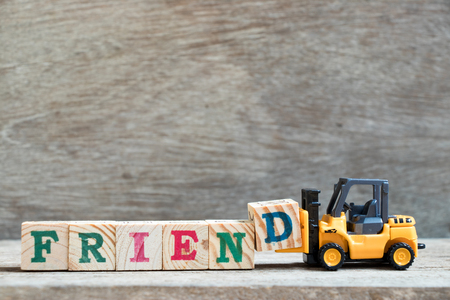 Toy forklift hold letter block D to complete word friend on wood backgroundの写真素材