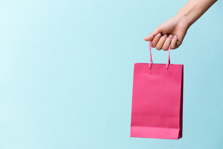 Hand of business woman hold pink shopping bag on blue concrete backgroundの写真素材
