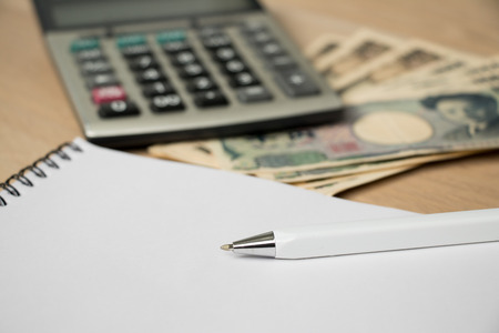 Blank note book with pen, japanese yen and calculator on wood table backgroundの写真素材