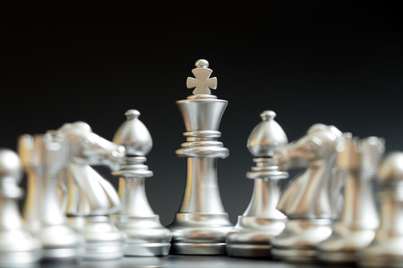 Silver king chess piece stand with bishop, knight, rook, pawn on black background (Concept for...