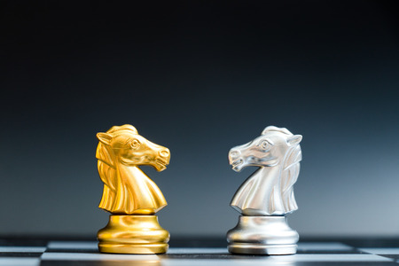 Gold and silver horse chess piece face in chessboard on black backgroundの写真素材