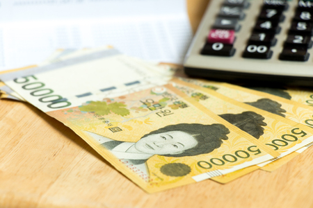 Blank note book with pen, calculator and south korea won (krw) banknote on wood table backgroundの写真素材