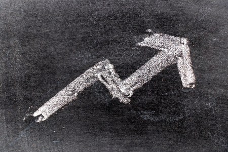 White color chak hand drawing in uptrend arrow shape on blackboard background (Concept of revenue, profit or cost increase, stock or business growth)の写真素材