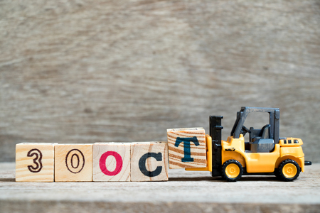 Toy forklift hold block T to complete word 30 Oct on wood backgroundの写真素材