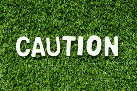 Alphabet letter in word caution on artificial green grass backgroundの写真素材