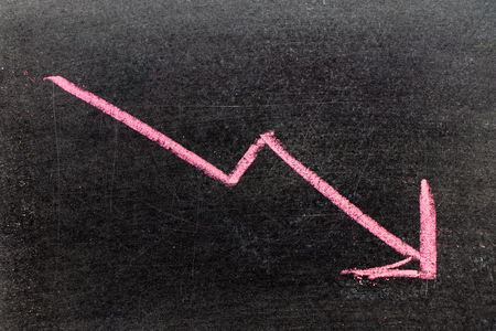 Red color hand drawing chalk in arrow down shape on black board background (Concept of stock decline, down trend of business, economy)の写真素材