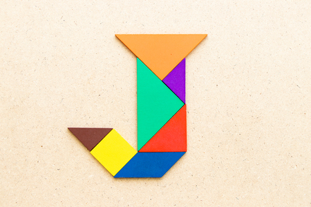 Tangram puzzle in alphabet letter J shape on wood backgroundの写真素材