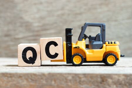 Toy forklift hold letter block c to complete word QC (Abbreviation of Quality Control) on wood backgroundの写真素材