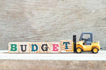 Toy forklift hold letter block t to complete word budget on wood backgroundの写真素材