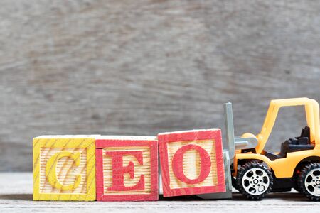 Toy forklift hold letter block O to complete word CEO (abbreviation of Chief Executive Officer) on wood backgroundの写真素材