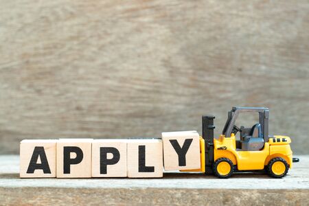 Toy forklift hold letter block y to complete word apply on wood backgroundの写真素材