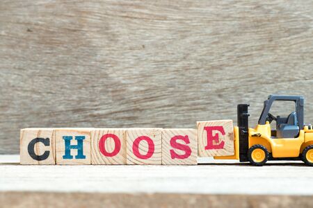 Toy forklift hold letter block e to complete word choose on wood backgroundの写真素材
