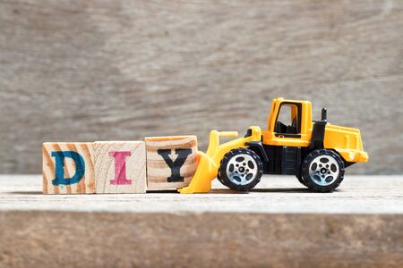 Toy bulldozer hold letter block Y to complete word DIY (abbreviation of do it yourself)  on wood backgroundの写真素材
