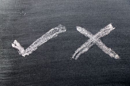 White color chalk hand drawing in check mark of right and wrong shape on black board background