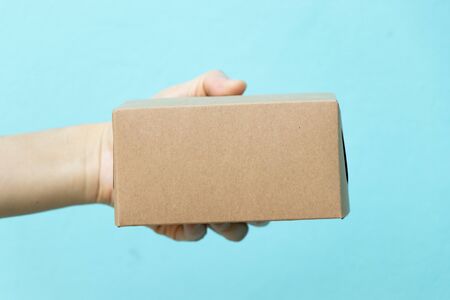 Woman hand hold the brown corrugated box on blue  wall background with copy space