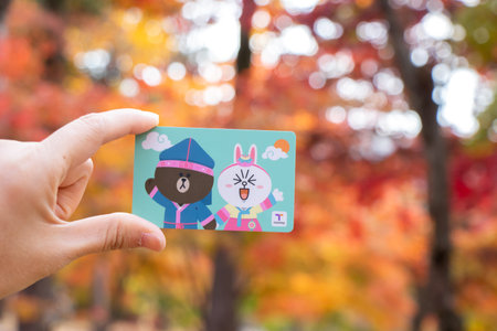 Seoul, South Korea- Oct 24, 2019 : Traveller hand hold t money card with line cartoon character on blur autumn background. T Money is a prepaid card for travelling with train, bus and shopping in South Koreaのeditorial素材