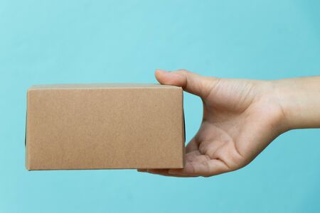 Woman hand hold the brown corrugated box on blue  wall background with copy space