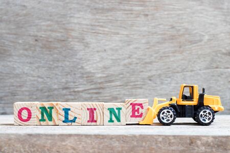 Toy bulldozer hold letter block e to complete word online on wood backgroundの写真素材