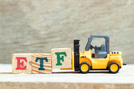 Toy forklift hold letter block to complete word ETF (abbreviation of Exchange Traded Fund) on wood backgroundの写真素材