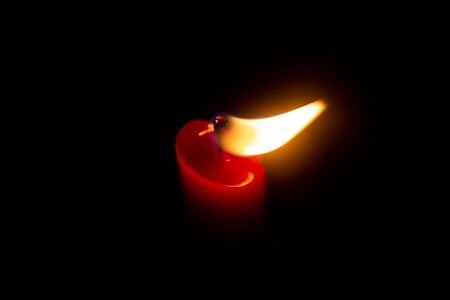 Red candle with yellow flame on black backgroundの写真素材