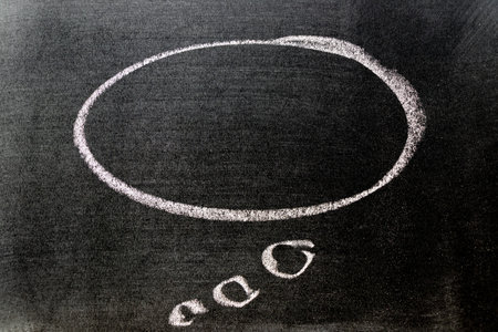 White color chalk hand drawing in round thinking bubble speech shape with blank space on black board backgroundの写真素材