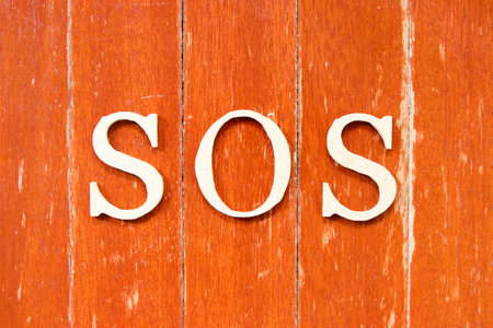 Alphabet letter in word SOS (abbreviation of save our soul/ship or sibling over shoulder) on old red color wood plate backgroundの写真素材