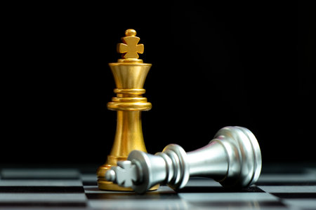 Gold king chess piece win over lying down silver king on black background