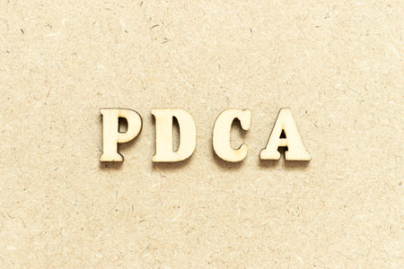Alphabet letter in word PDCA (Abbreviation of plan do check act) on wood backgroundの写真素材