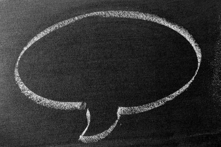 White color chalk hand drawing in round bubble speech shape with blank space on blackboard or...