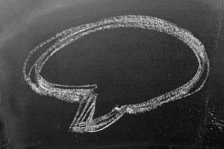 White color chalk hand drawing in round bubble speech shape with blank space on blackboard or...