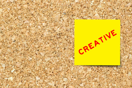 Yellow note paper with word creative on cork board background with copy spaceの写真素材
