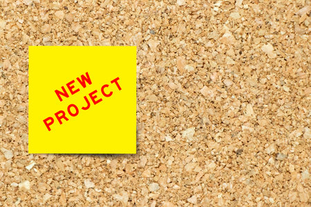 Yellow note paper with word new project on cork board background with copy spaceの写真素材