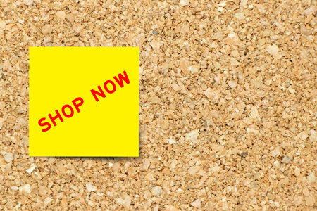 Yellow note paper with word shop now on cork board background with copy space
