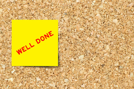 Yellow note paper with word well done on cork board background with copy space