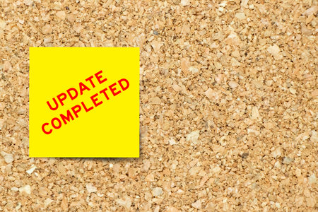 Yellow note paper with word update completed on cork board background with copy spaceの写真素材
