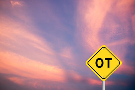 Yellow transportation sign with word OT (abbreviation for overtime) on violet color sky backgroundの写真素材