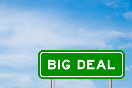 Green color transportation sign with word big deal on blue sky with white cloud backgroundの写真素材