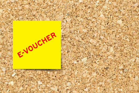 Yellow note paper with word e-voucher on cork board background with copy spaceの写真素材