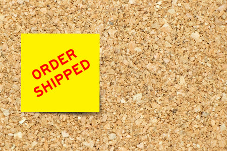 Yellow note paper with word order shipped on cork board background with copy space