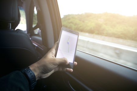 male driver sitting in the car and holding black mobile smart phone with map gps navigation...