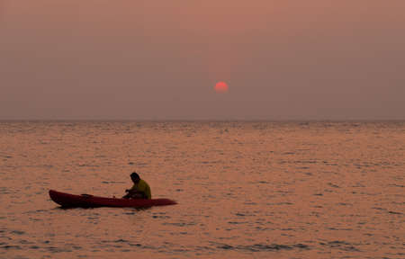 Silhouette of a man rowing in the canoe at sunsetの写真素材