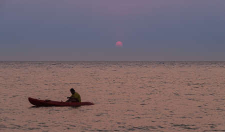 Silhouette of a man rowing in the canoe at sunsetの写真素材