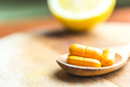 Slice of lemon and vitamin C pills in the wooden spoon on the tableの写真素材