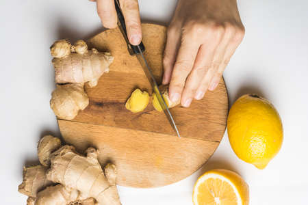 Caucasian woman's hand is cutting a ginger root. On top, flat lay.の写真素材